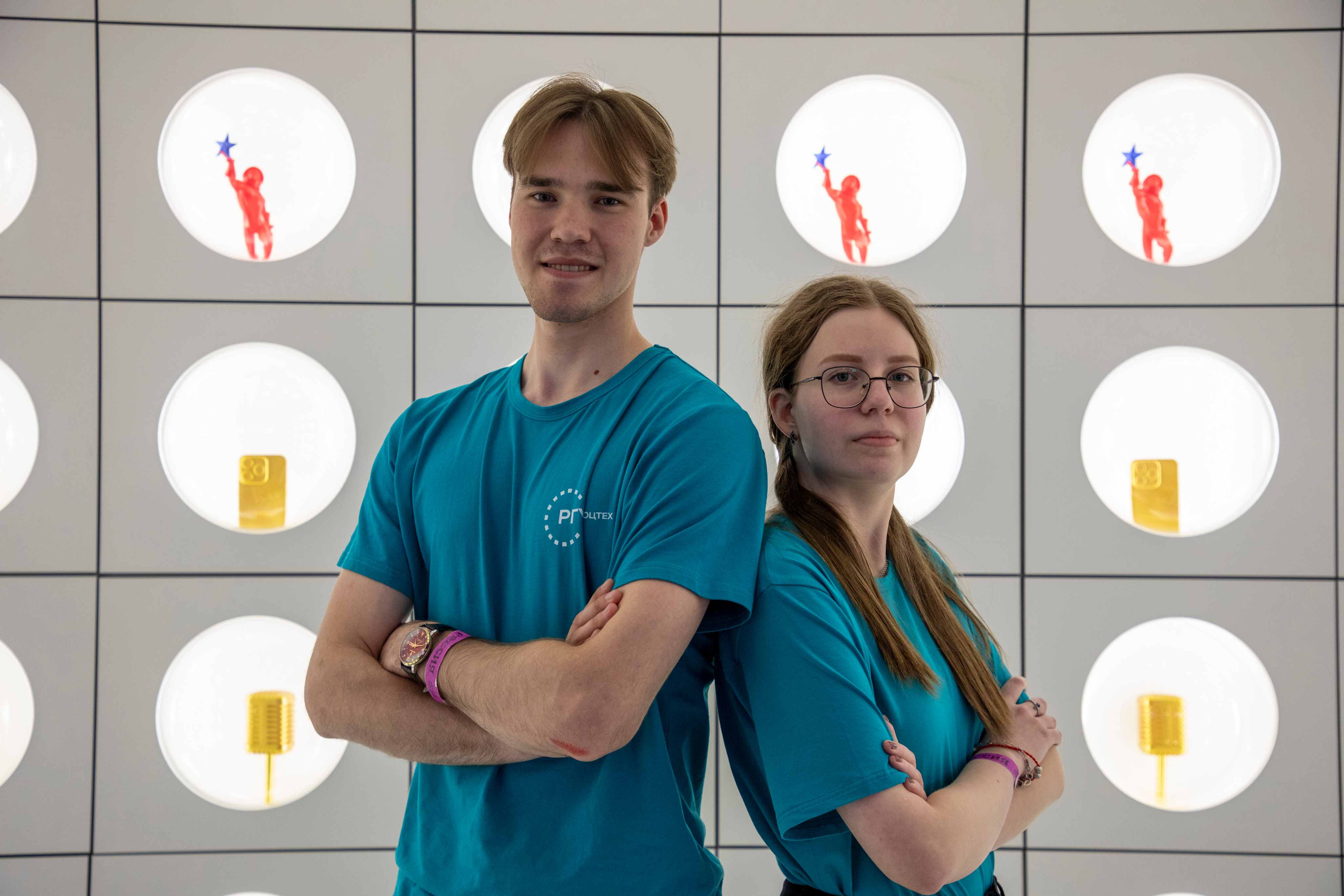 Deux étudiants en t-shirts turquoise identiques RSU ST posent devant un mur lumineux moderne.